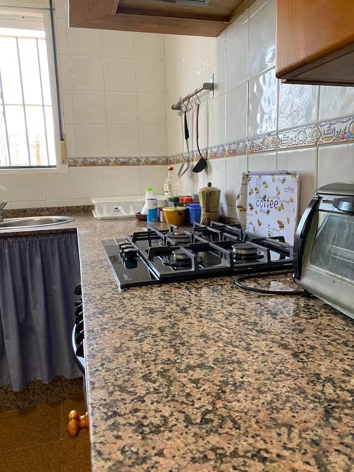 Encimera de cocina con estufa de gas, tostadora y utensilios. Encimera de granito marrón y beige.