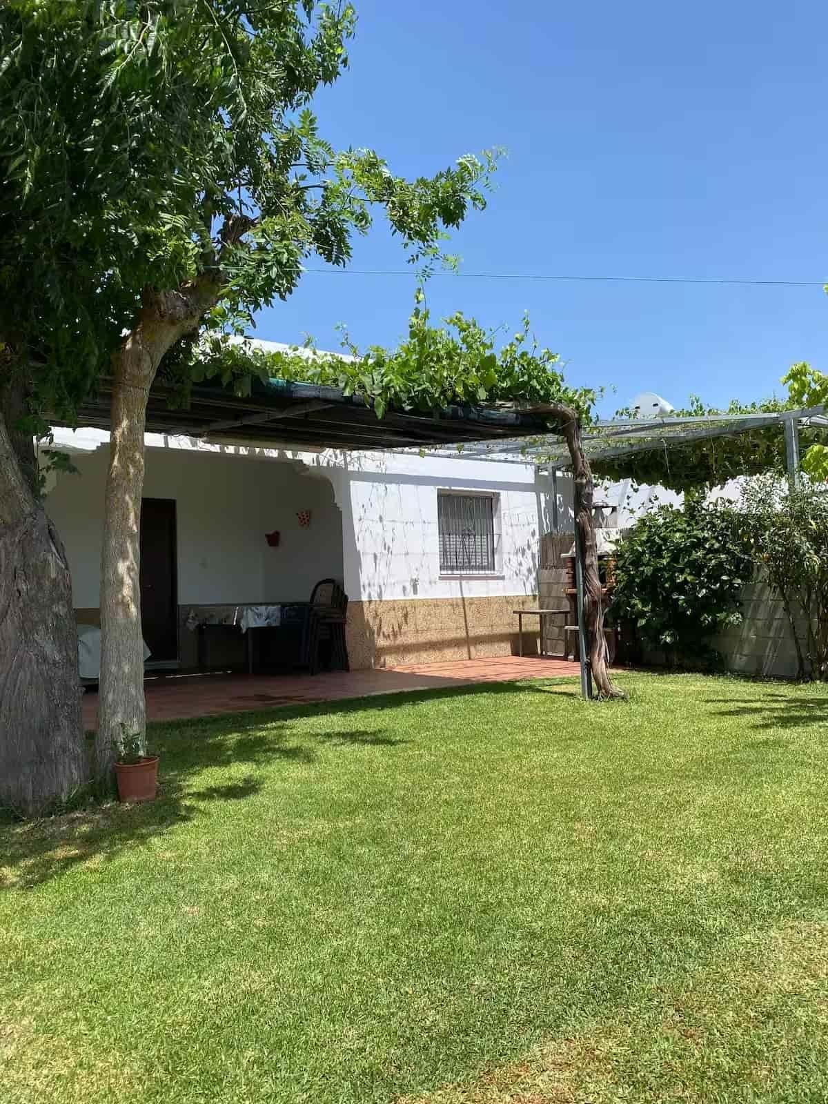 Un pequeño edificio blanco con un patio cubierto y un césped verde.
