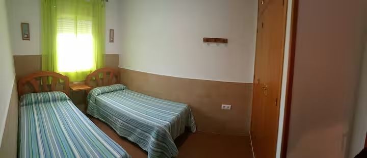 Un dormitorio con dos camas individuales, cortinas verdes y un armario de madera.