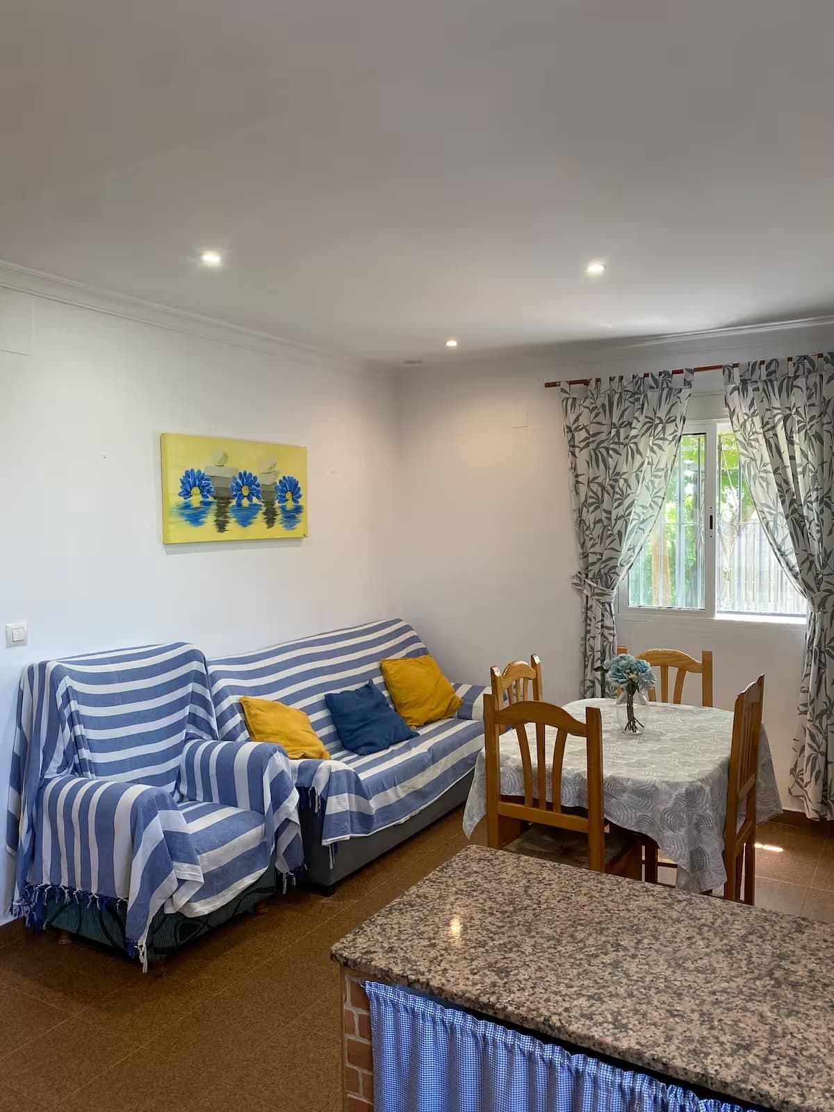 Sala de estar con sofá de rayas azules y blancas, mesa de comedor y cortinas florales.