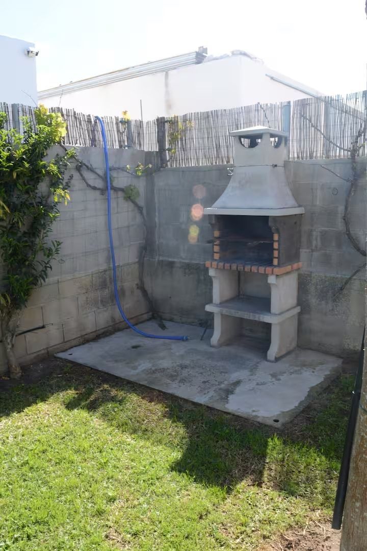 Patio trasero de concreto con parrilla, césped y cerca de concreto.