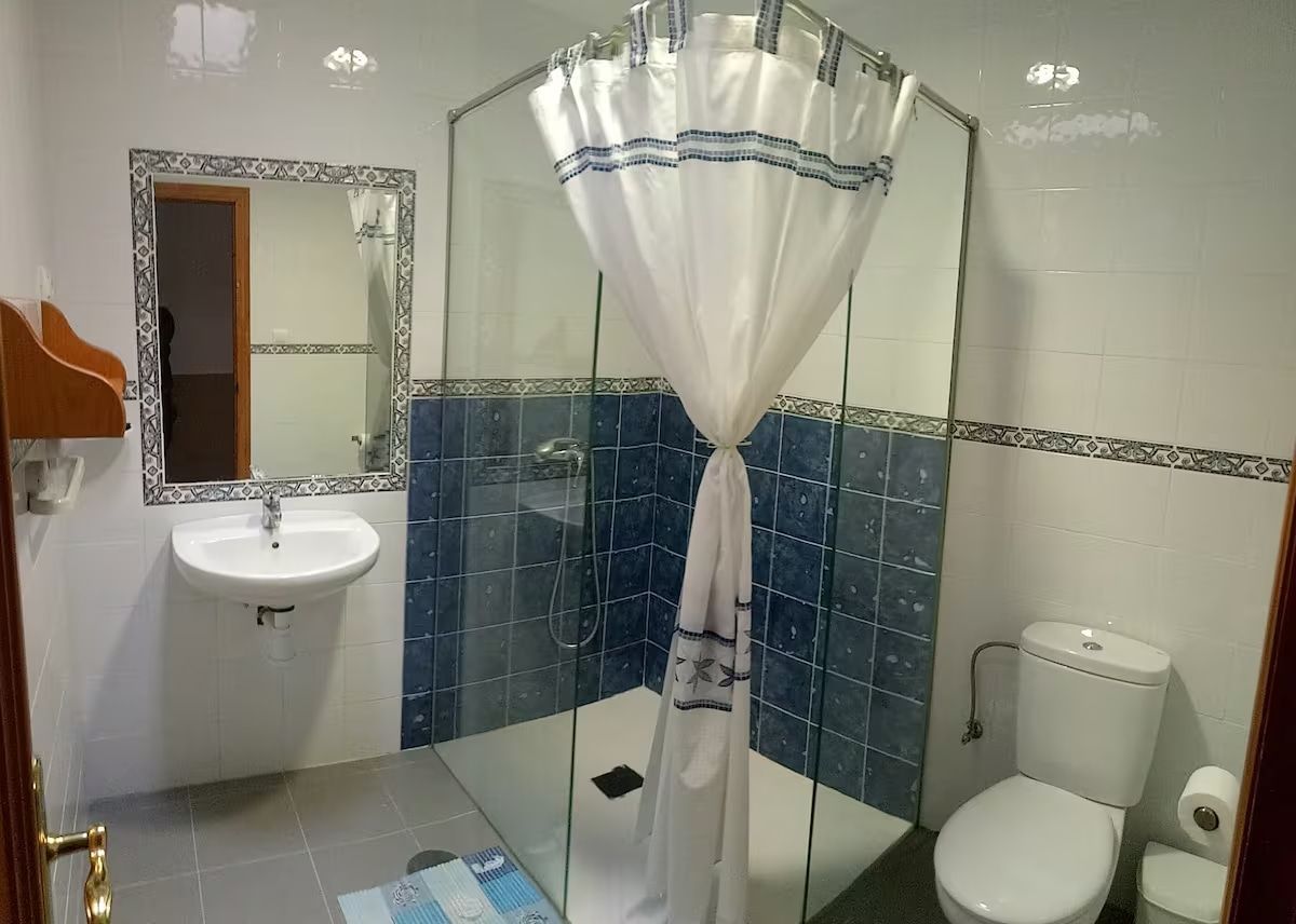 Baño con ducha, inodoro, lavabo y espejo. Detalles de azulejos azules y blancos.