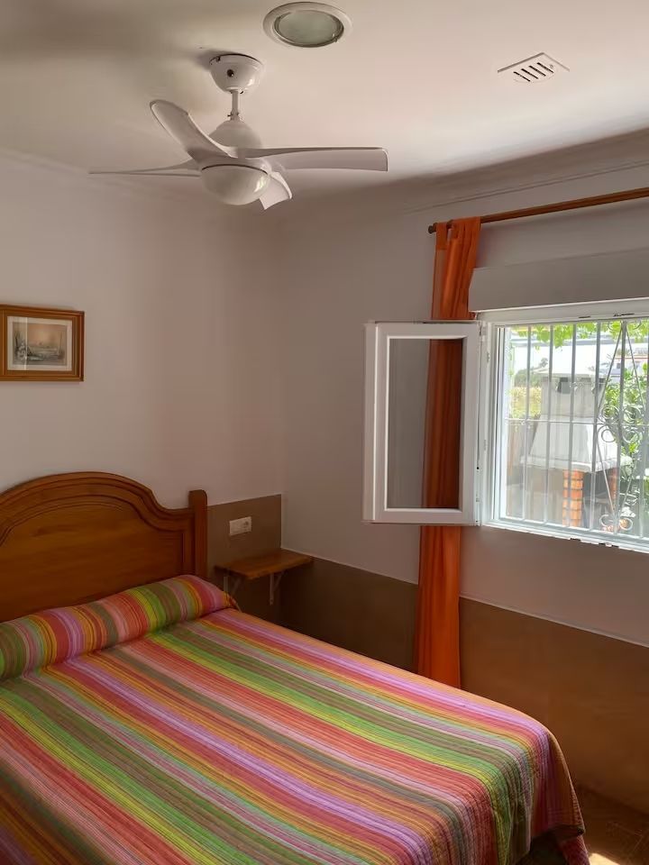 Dormitorio con cama, ventana, ventilador de techo y cortinas naranjas.