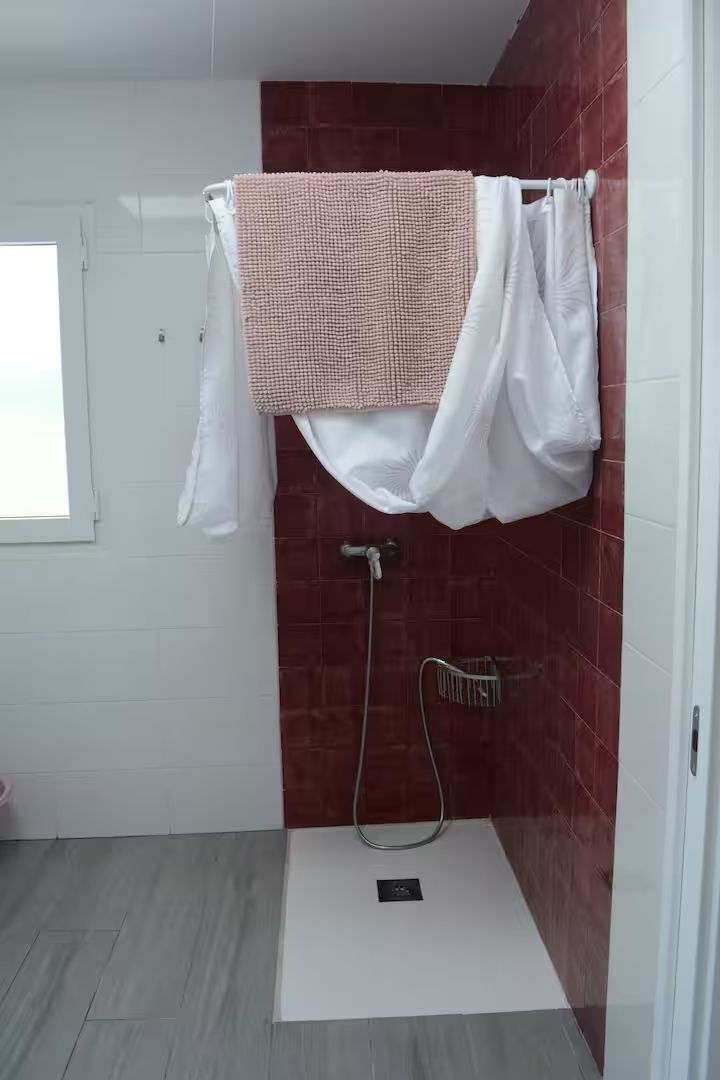 Cabina de ducha con pared de azulejos rojos, suelo de baldosas blancas y cortina de ducha.