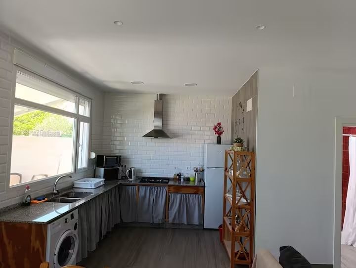 Cocina con salpicadero de ladrillo blanco, electrodomésticos, gabinetes de madera y ventana grande.