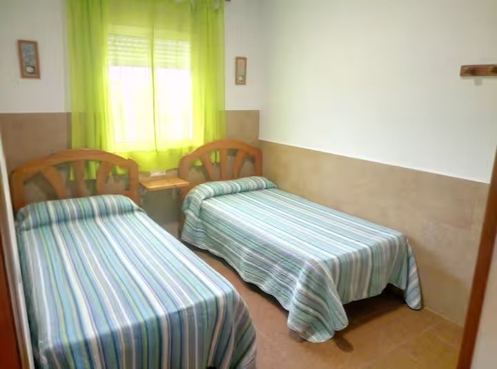 Dos camas individuales en una habitación con ventana, paredes color canela y blancas y cortinas verdes.