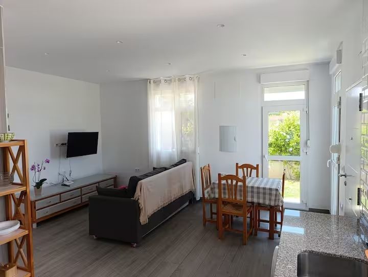 Sala de estar con un sofá gris, TV, mesa de comedor y una puerta que da al patio trasero.