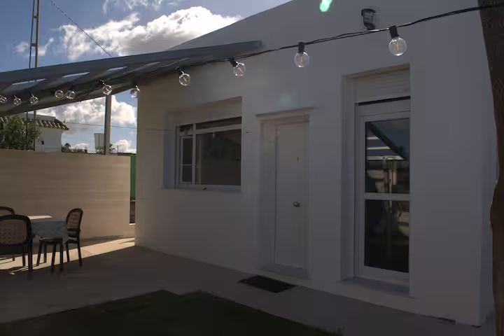 Exterior de edificio blanco con luces de cadena, ventana, puerta y muebles de patio a la luz del día.
