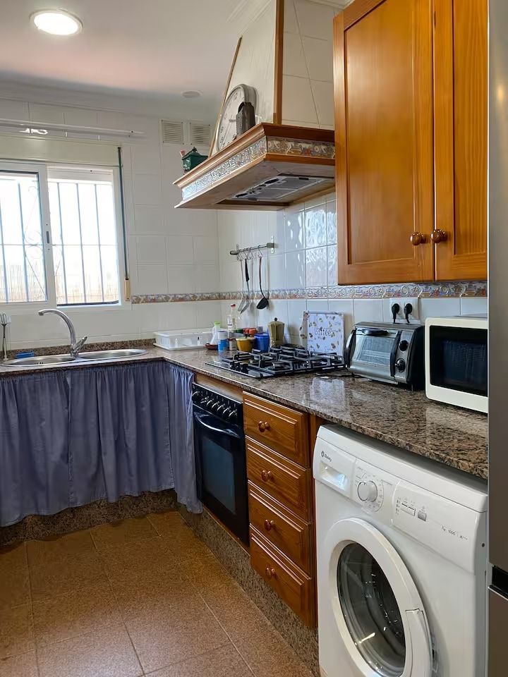 Cocina con gabinetes de madera, estufa, microondas y lavadora. 