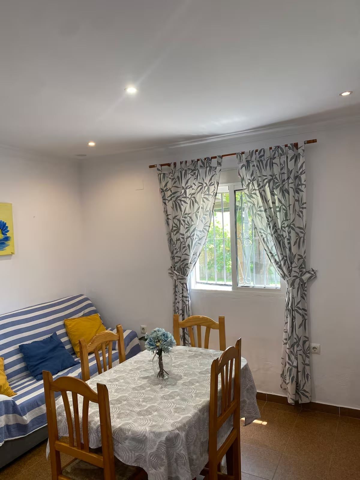 Un pequeño comedor con mesa, sillas, sofá y una ventana con cortinas estampadas.