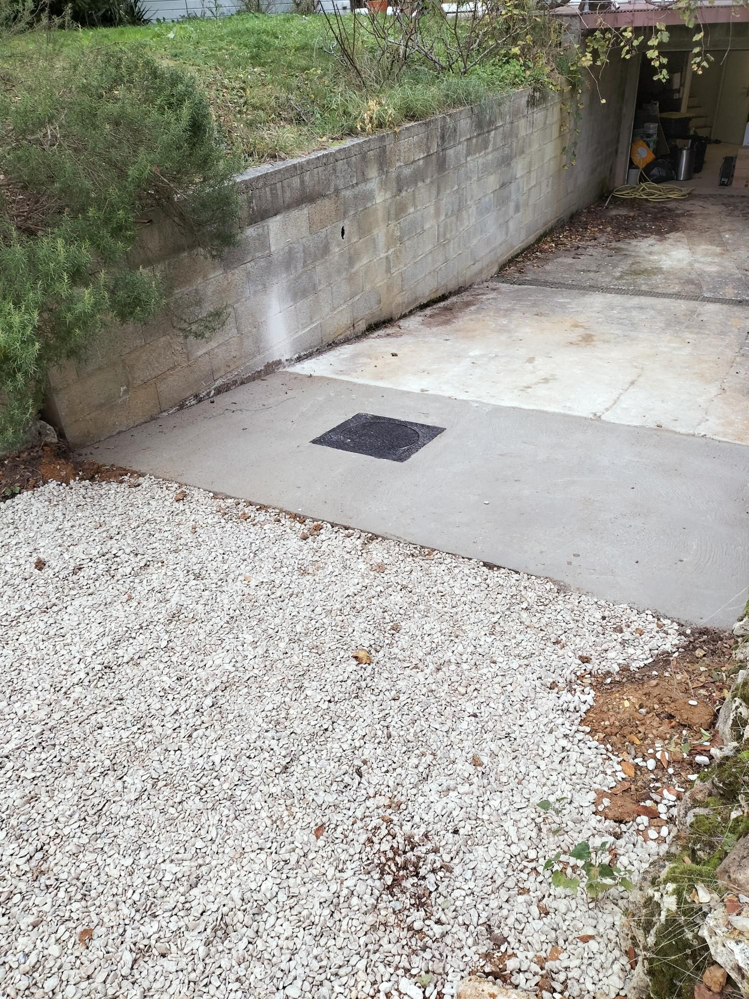 Allée en gravier en pente, avec une dalle en béton, une grille d’évacuation et un mur de soutènement le long d’un passage étroit