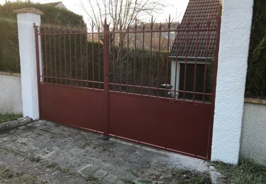 Portail rouge fermé en métal entre des piliers blancs à l’entrée d’une allée