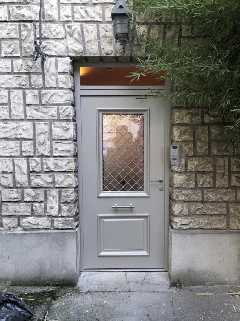 Porte d’entrée grise avec une fenêtre à petits carreaux en losange, intégrée dans un mur extérieur en pierre