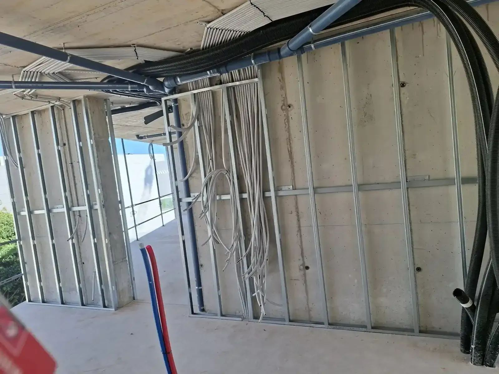 Estructura de pared y cableado a la vista en una habitación sin terminar con aislamiento y tuberías de conducto.