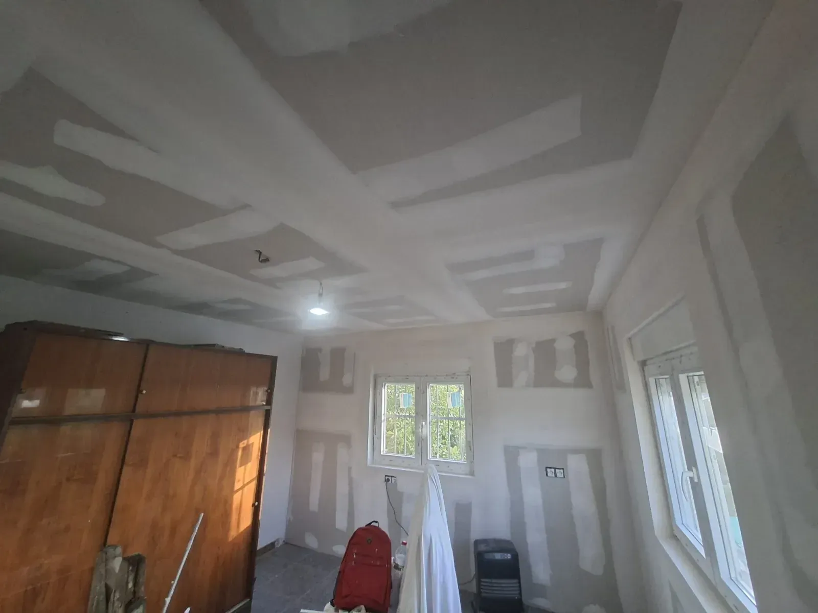 Habitación vacía en proceso de renovación con techo de pladur, armario de madera, sillas.