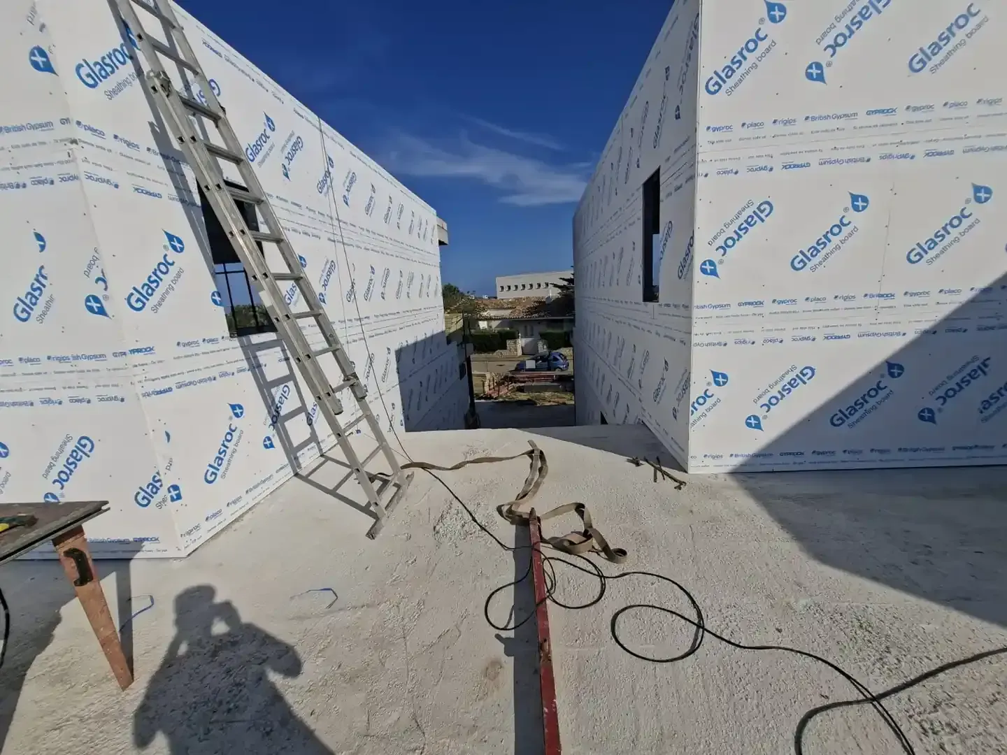 Interior de una obra en construcción con paredes aisladas, una escalera y cables eléctricos.
