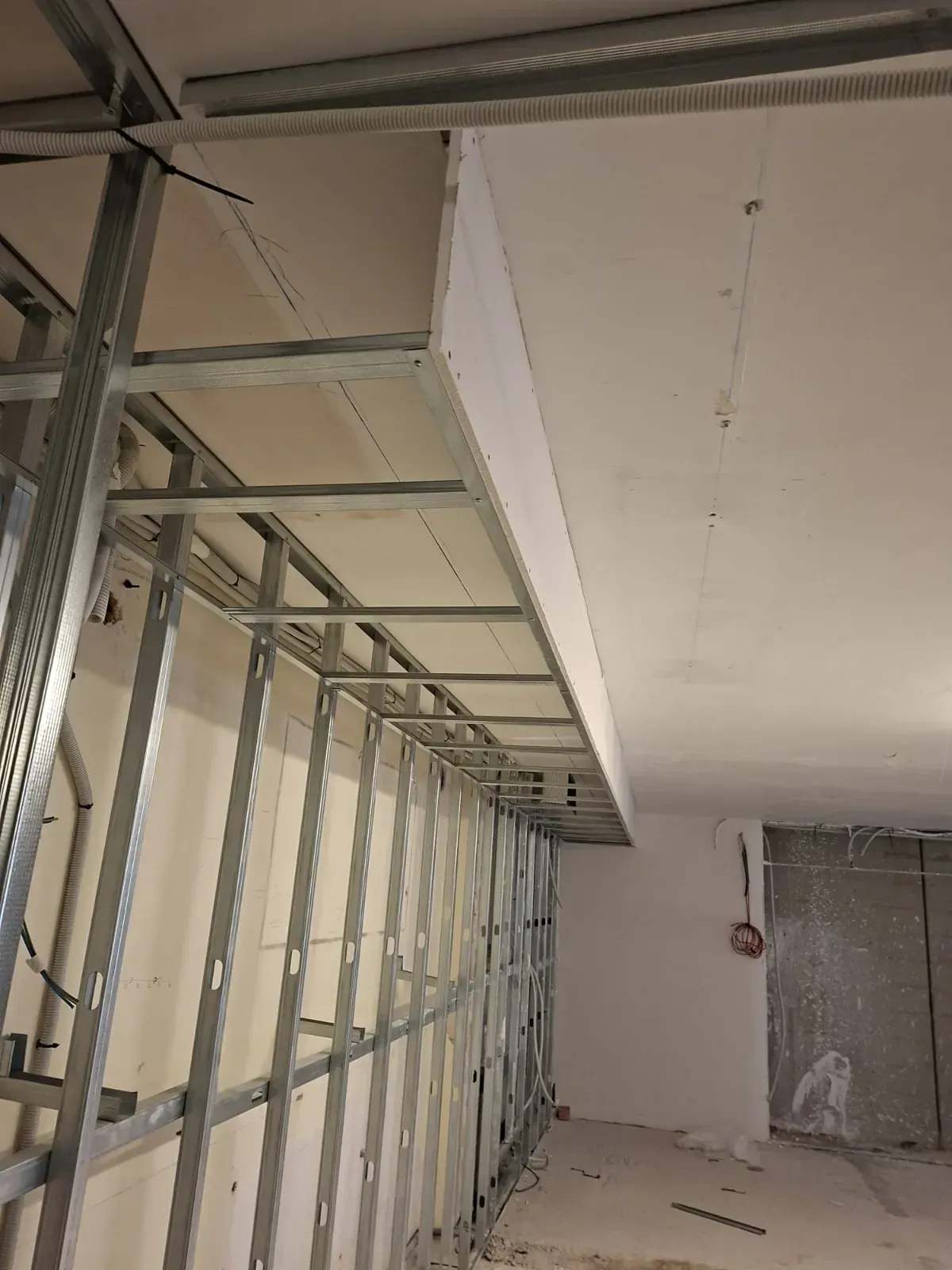 Habitación sin terminar con estructura metálica a la vista, paneles de yeso y un piso de concreto en construcción.