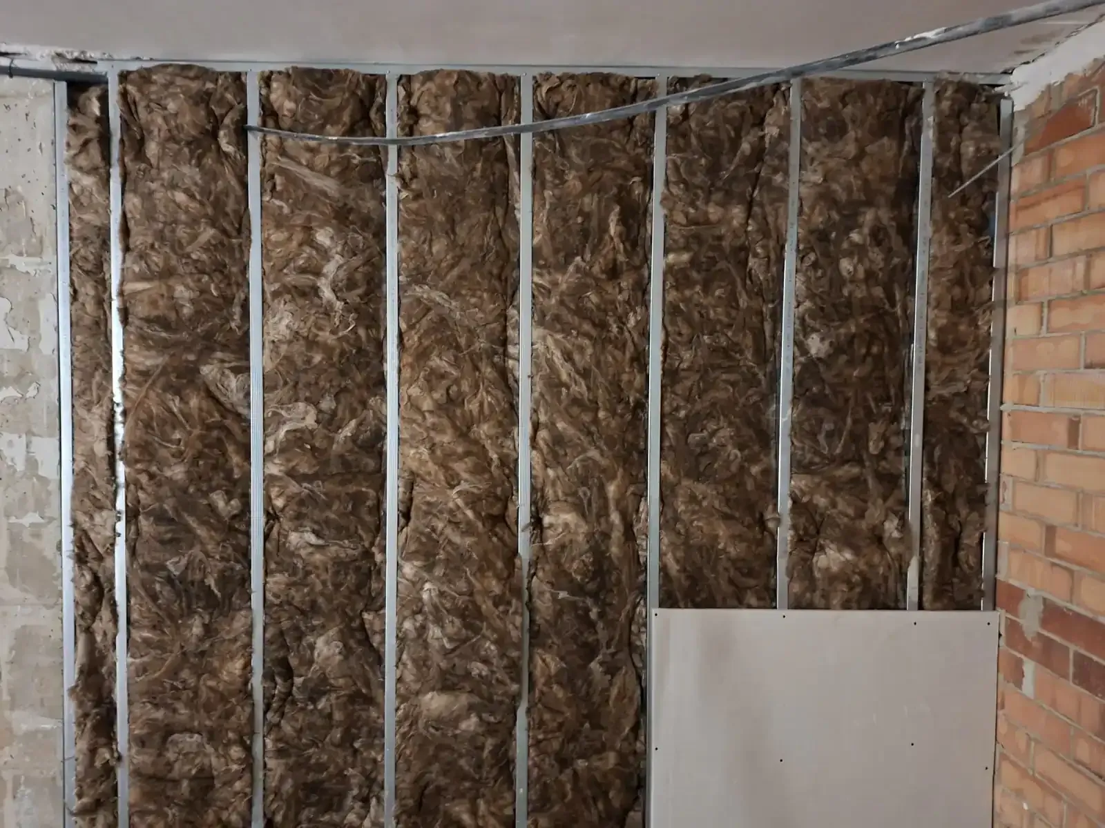 Pared aislada con estructura de montantes y cableado blanco en una habitación sin terminar.
