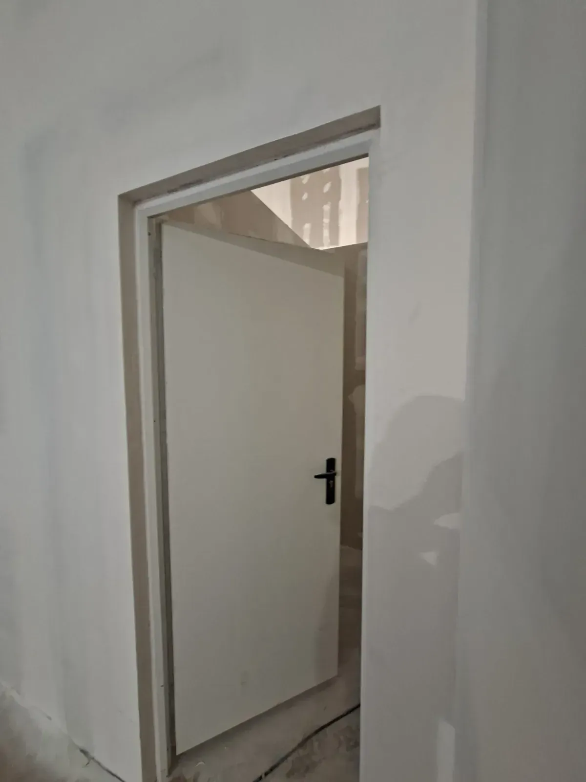 Puerta blanca parcialmente abierta en un pasillo interior sencillo con manija negra.