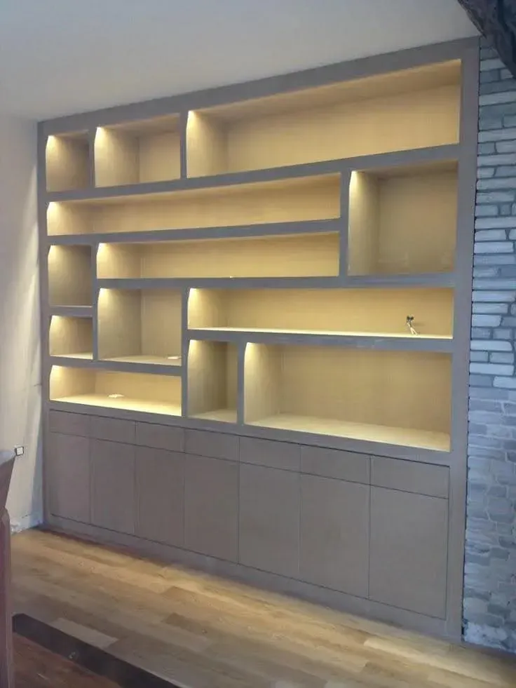 Estanterías empotradas en la pared con iluminación cálida sobre armarios de madera clara en una habitación moderna.