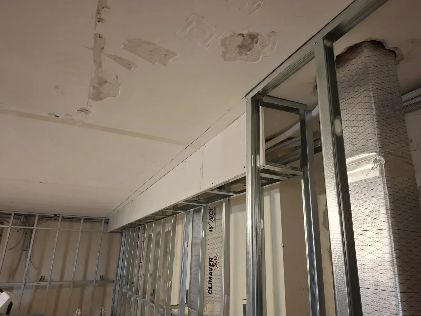 Habitación parcialmente renovada con estructura de pared metálica, techo a la vista y marco de puerta corredera de cristal.