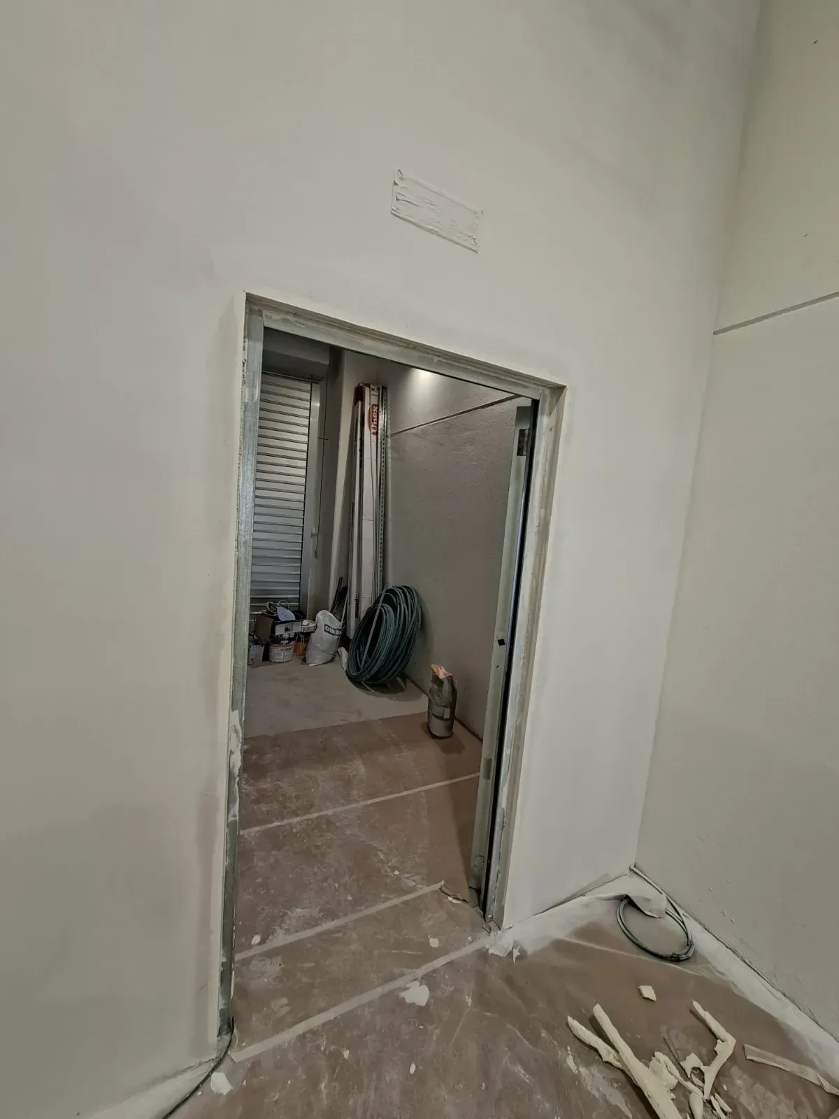 Pasillo que da a una habitación en obras, con suelo de baldosas, paredes blancas y herramientas en el suelo.