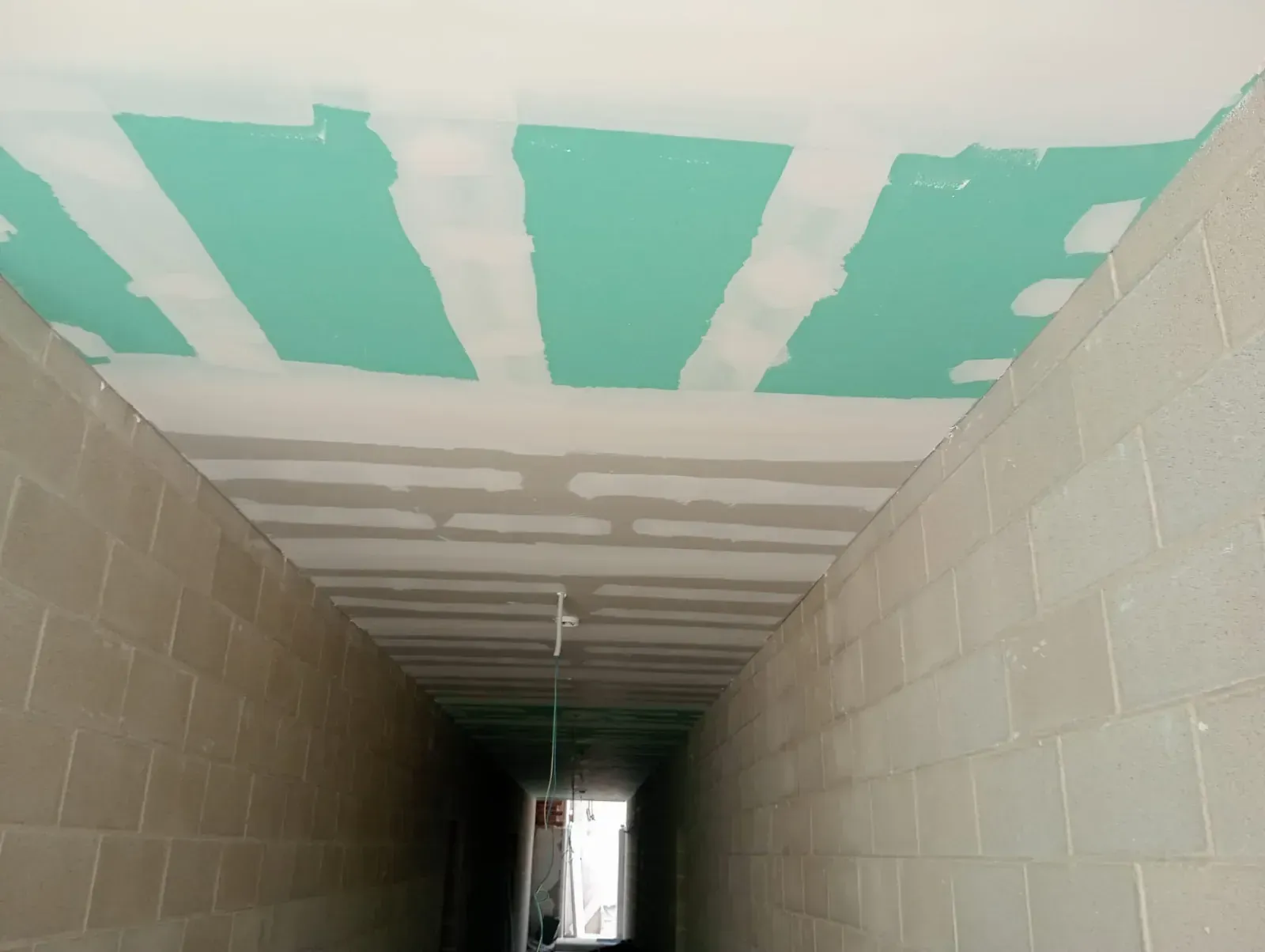 Un pasillo largo y oscuro con paredes de bloques de hormigón sin terminar y un techo remendado en verde y blanco.