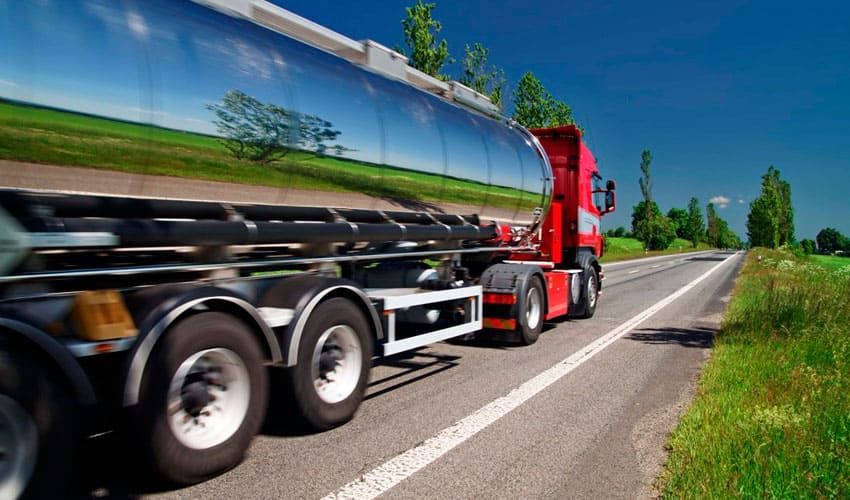 Un camión semirremolque circula por una carretera al lado de un campo.
