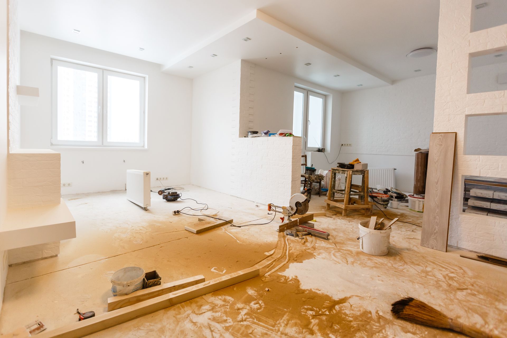 Salon inachevé avec des cloisons sèches, des outils et des matériaux de construction sur un sol poussiéreux.