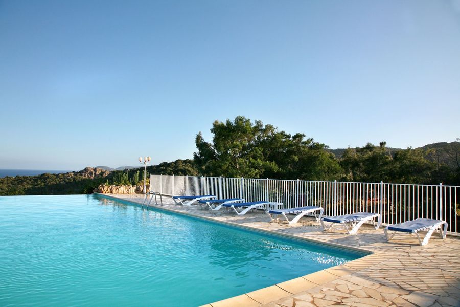 Piscine bleue bordée de chaises longues blanches et d'une clôture blanche donnant sur la mer au coucher du soleil