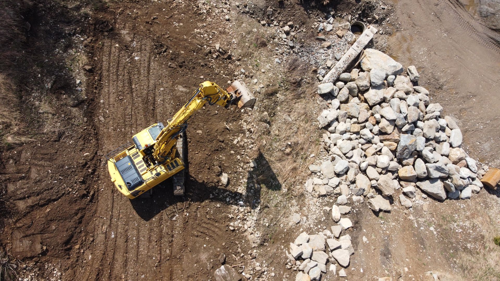 Une pelleteuse jaune déblaye de la terre à côté d'un tas de roches blanches sur un chantier de construction.
