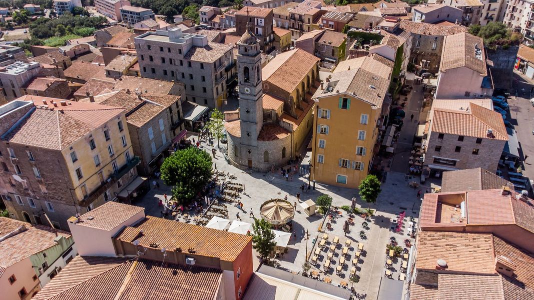 Vue aérienne d'une ville historique avec des toits de tuiles rouges et une place centrale animée.