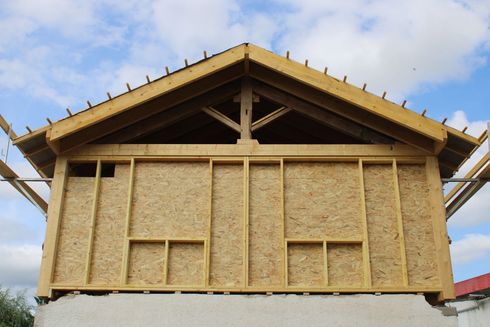 Maison en construction, avec charpente en bois apparente et toit à pignon sur fond de ciel nuageux
