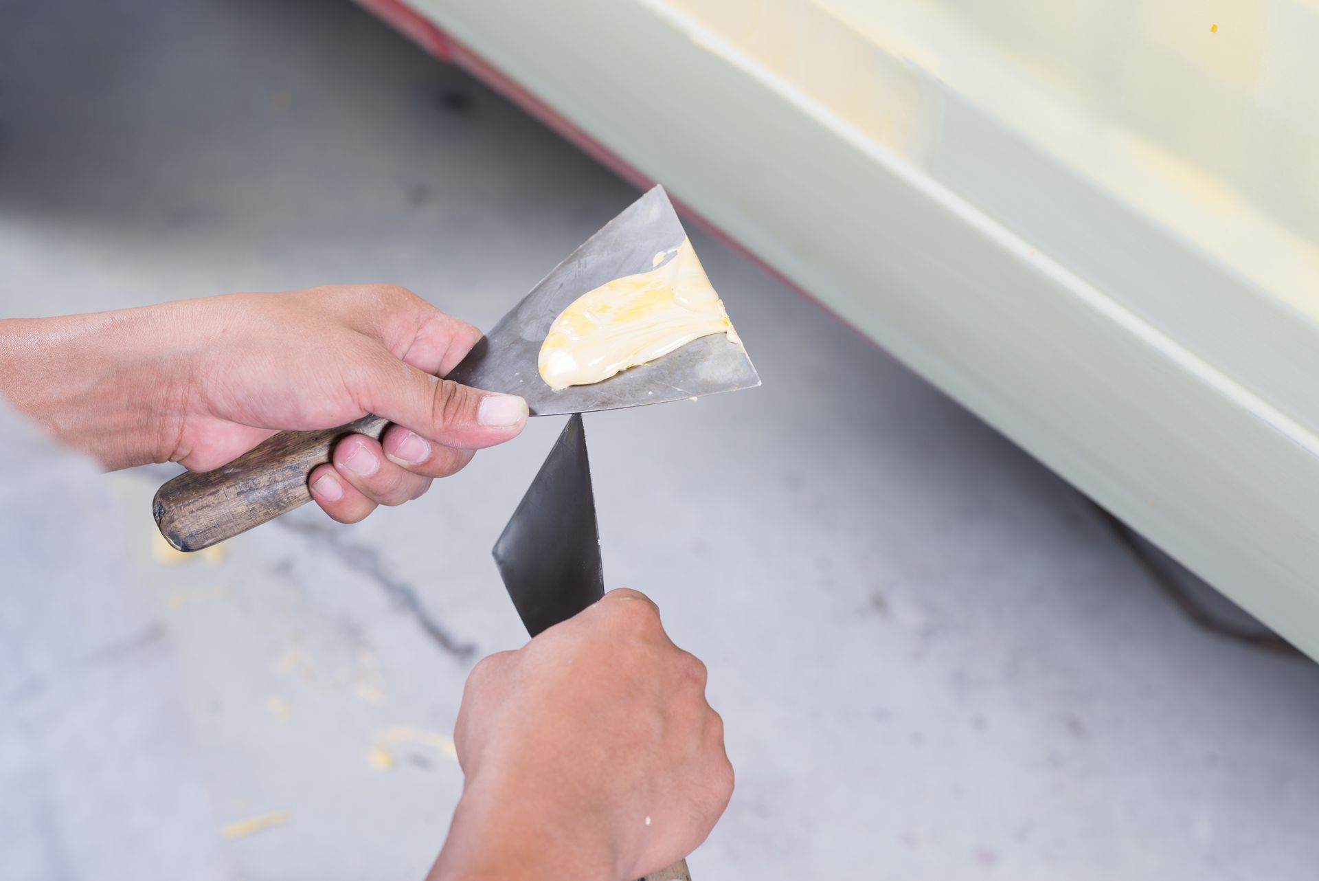 Des mains appliquent du mastic sur le panneau latéral d'une voiture à l'aide d'un couteau à mastic.