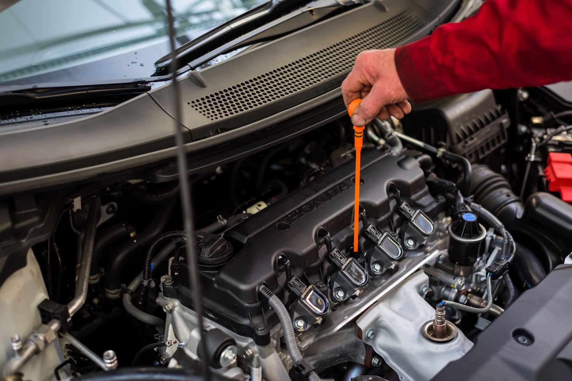 Personne vérifiant le niveau d'huile moteur de sa voiture à l'aide de la jauge.
