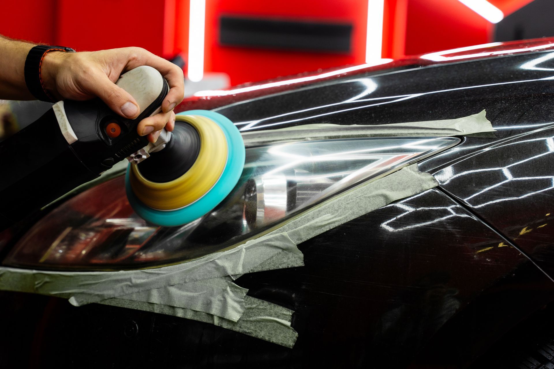 Une personne polit un phare de voiture avec un outil de polissage.