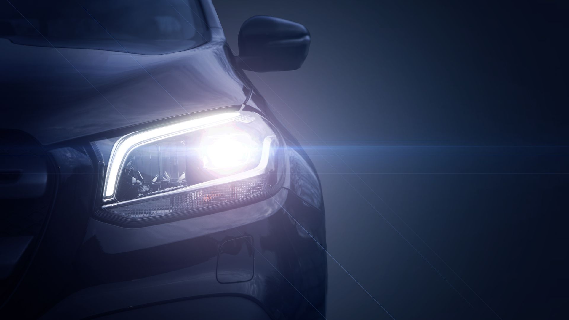 Phare d'une voiture sombre allumé la nuit, émettant une lumière blanche éclatante.