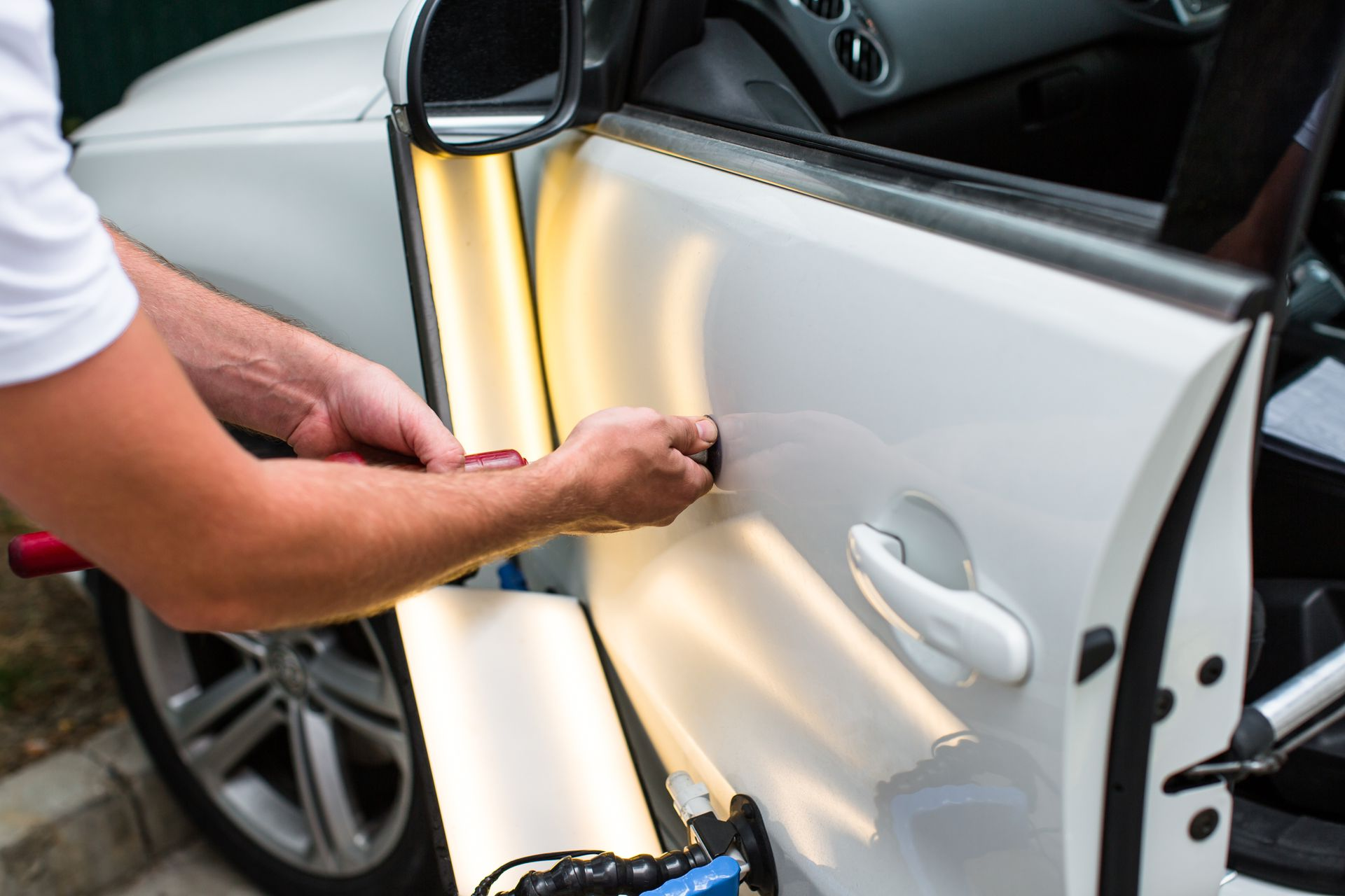 Une personne utilise des outils pour réparer une bosse sur la portière d'une voiture blanche.