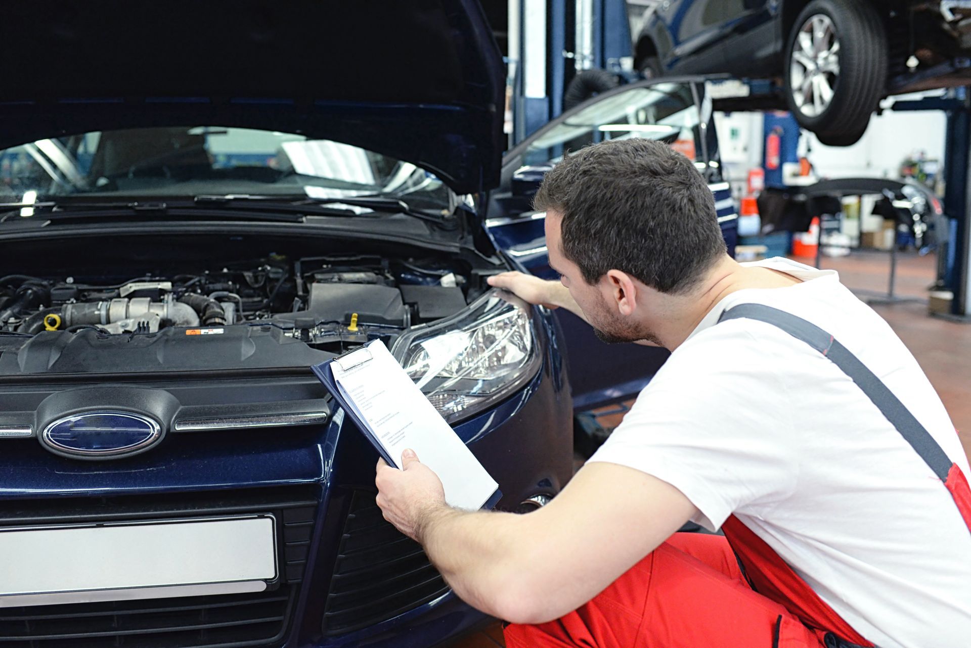 Un mécanicien inspecte le moteur d'une voiture avec un bloc-notes dans un atelier de réparation automobile.