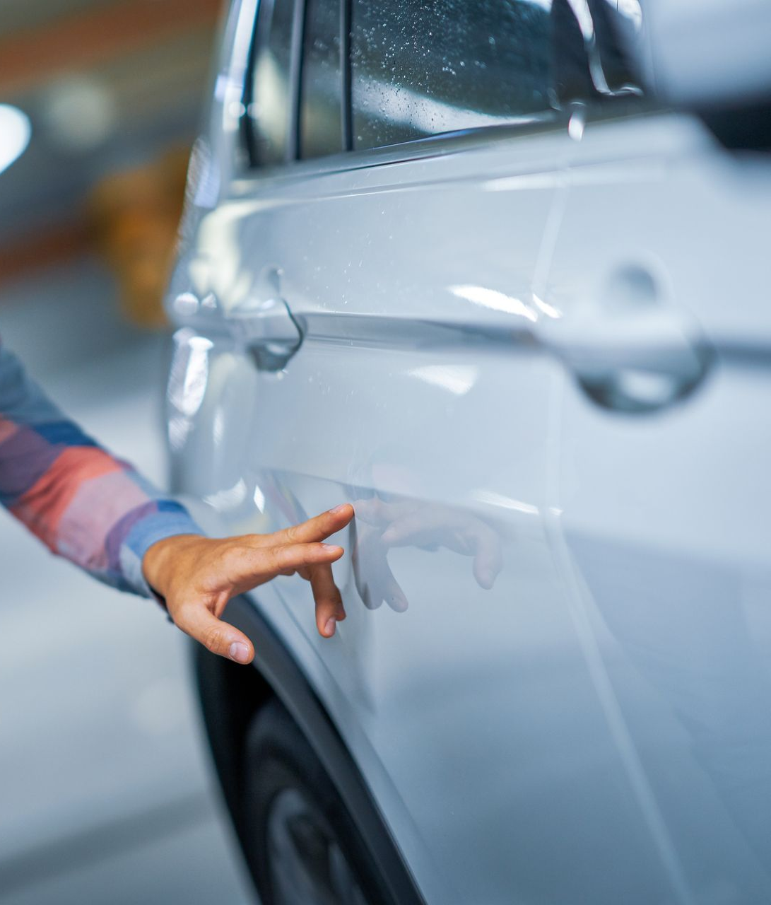 La main d'une personne touche le côté d'une voiture argentée, probablement pour vérifier s'il y a des dommages, dans un parking souterrain.