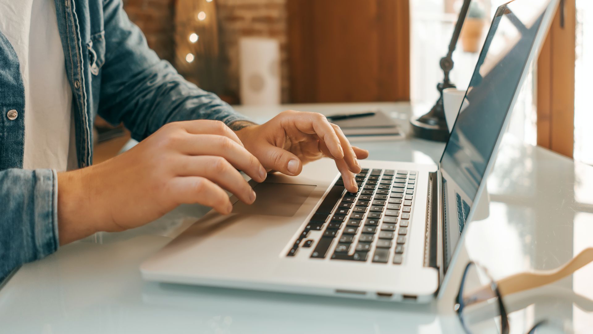 Personne tapant sur un ordinateur portable à un bureau, portant des lunettes.