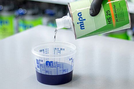 Verser à la main du diluant à peinture d'une bouteille verte et blanche dans un verre doseur contenant de la peinture bleue.