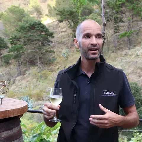 Un hombre con un chaleco negro sostiene una copa de vino.