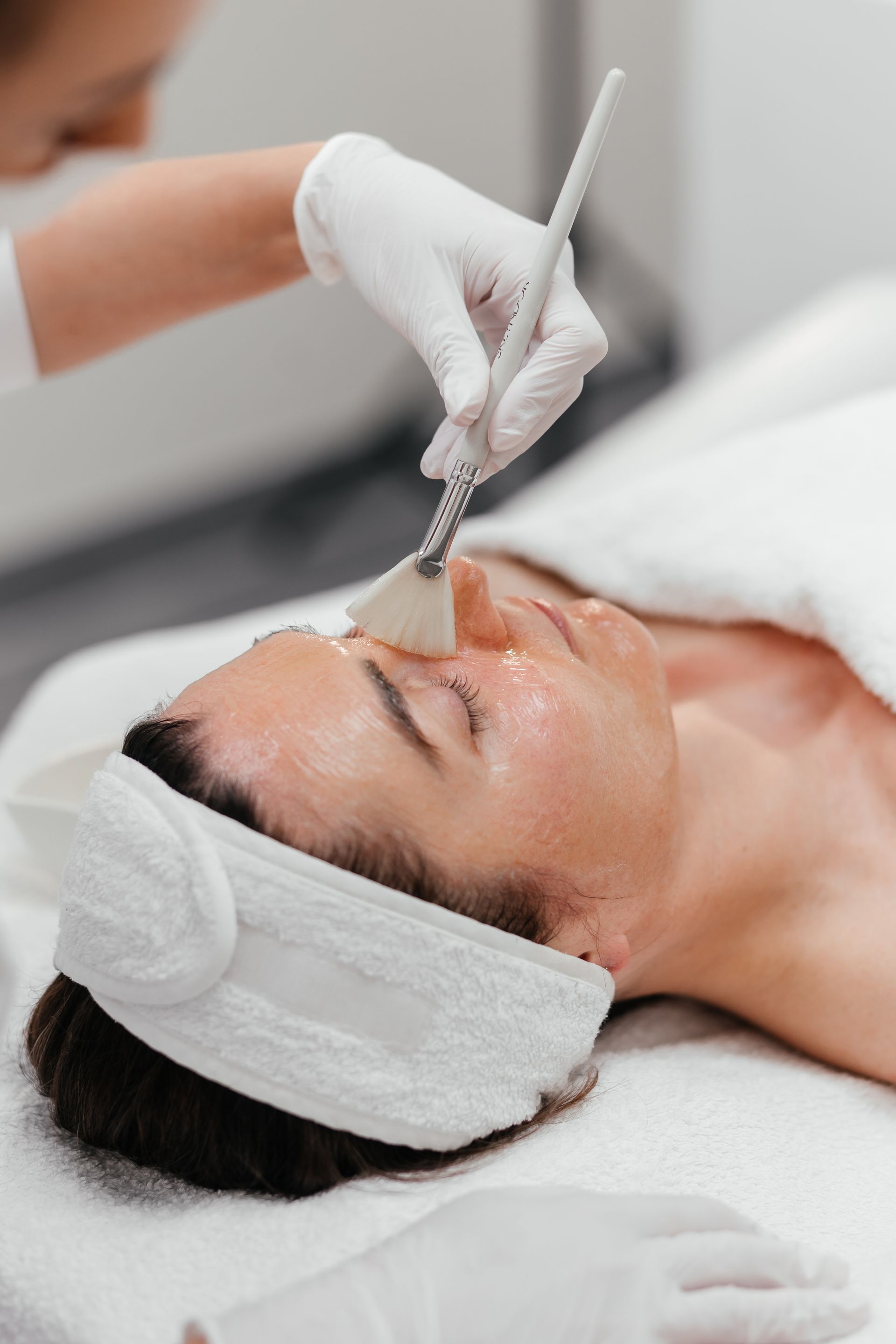 Une personne reçoit un soin du visage. Une esthéticienne gantée applique le produit au pinceau.