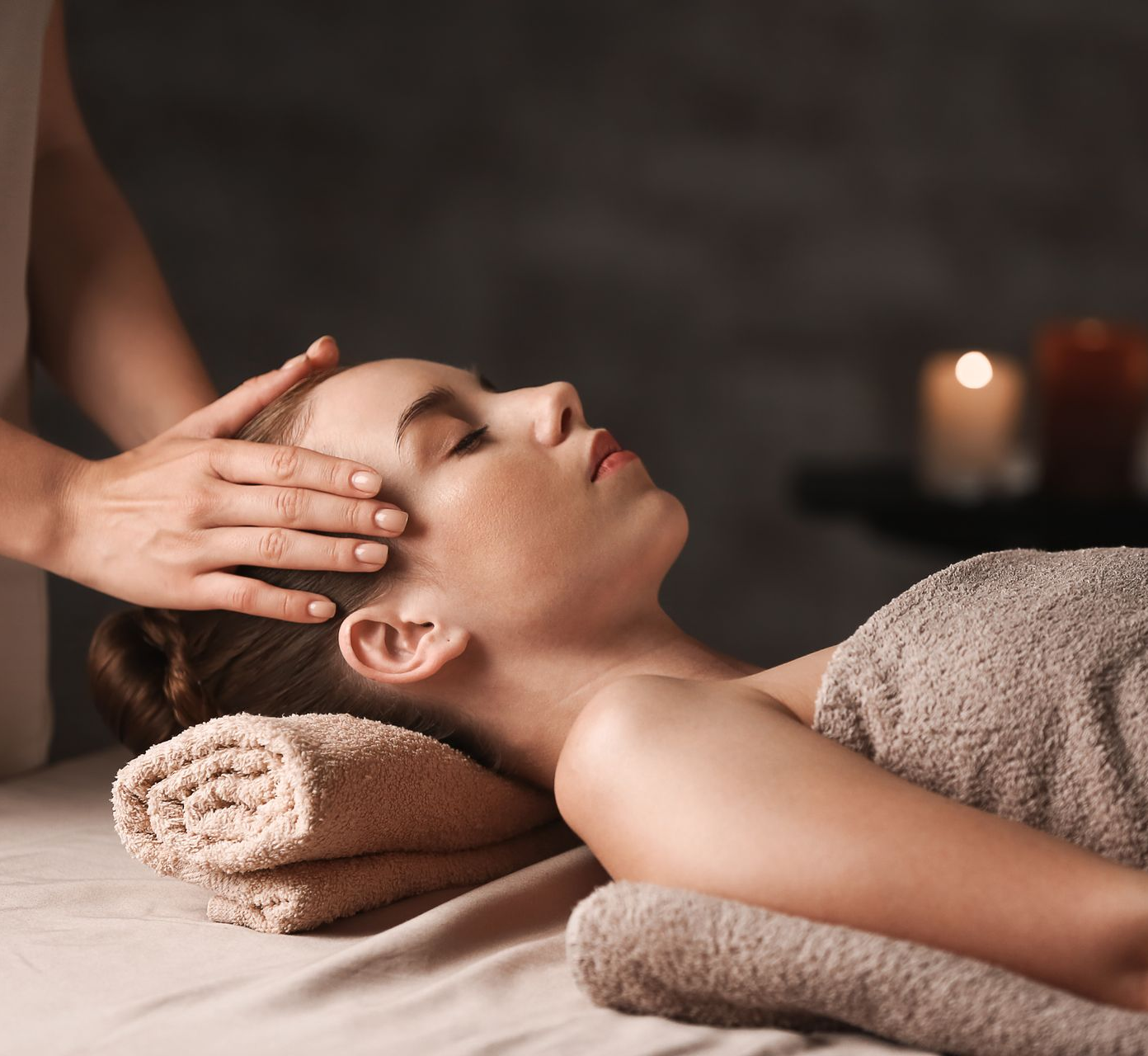 Femme recevant un massage crânien, les yeux fermés, allongée sur des serviettes.