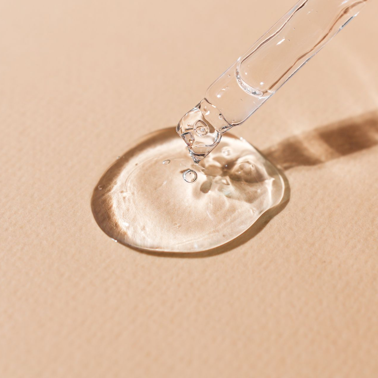 Gouttelette de sérum transparente provenant d’une pipette sur une surface beige.