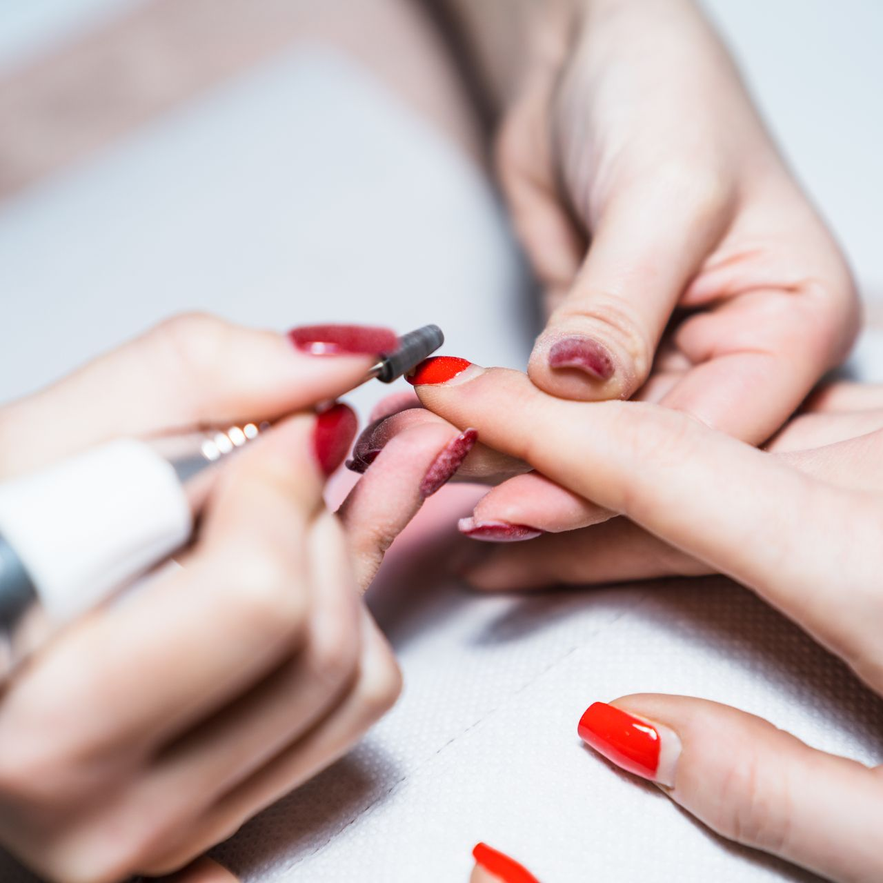 Mains recevant une manucure, utilisant une perceuse à ongles pour façonner les ongles, vernis à ongles rouge.