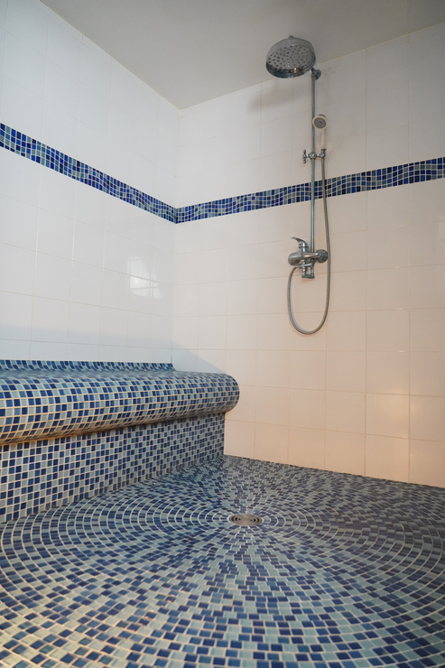 Douche carrelée bleue avec banc intégré, murs blancs avec garniture bleue et pomme de douche chromée.