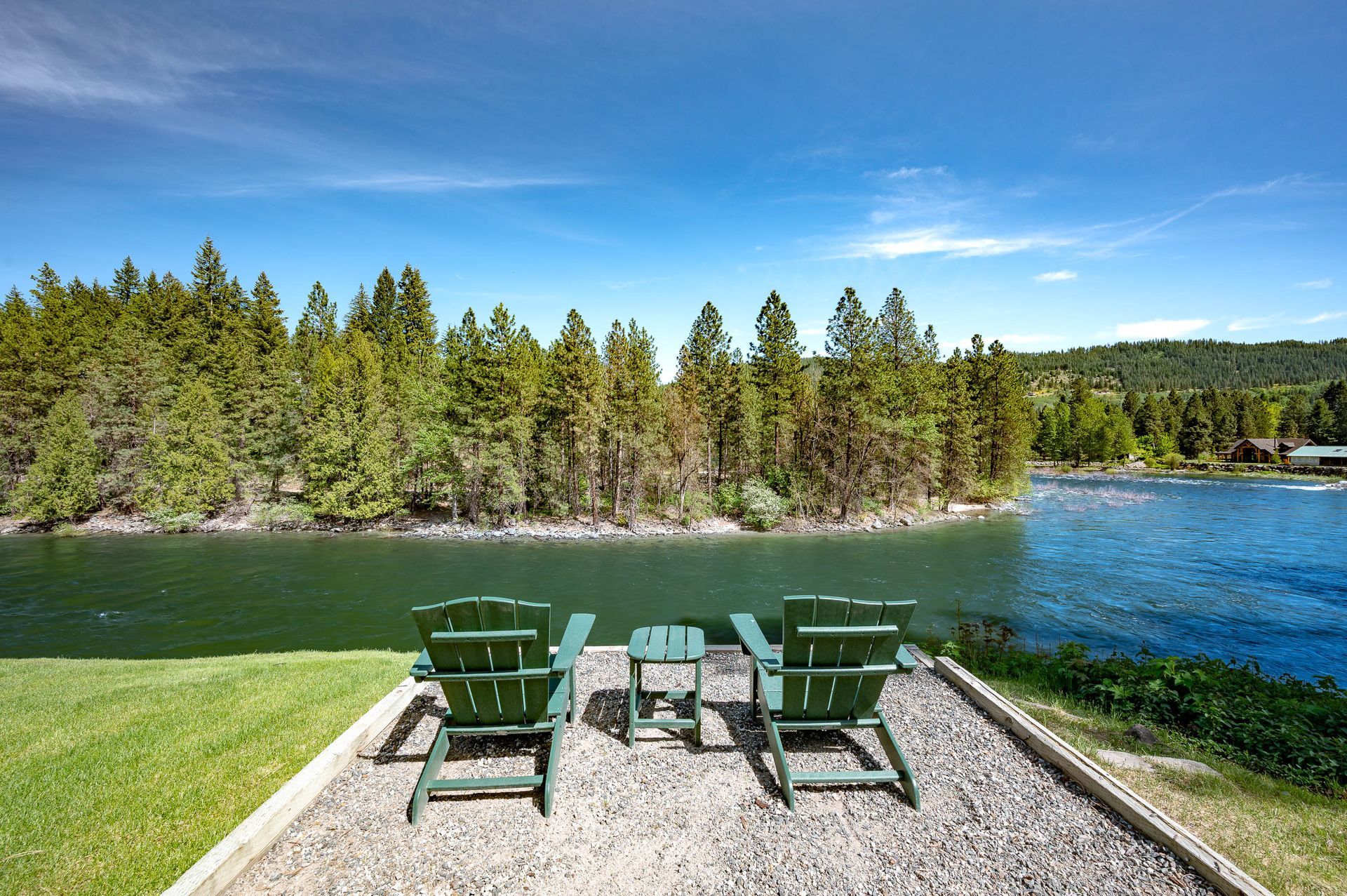 Two green chairs are sitting on a gravel patio overlooking a lake.
