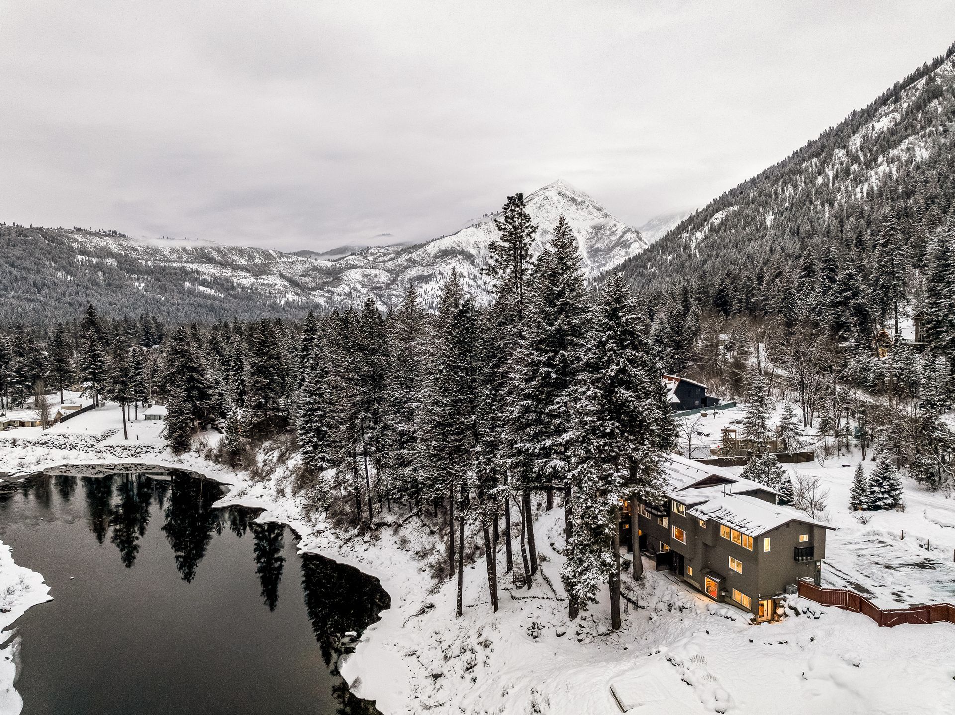 An aerial view of a house surrounded by snow covered trees and a lake.